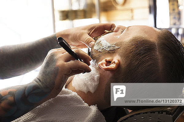 Ausgeschnittenes Bild eines Kunden  der sich beim Friseur rasiert