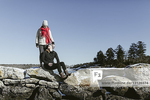Freundinnen auf Felsen gegen den klaren Himmel im Park im Winter
