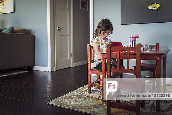 Full length of girl sitting on chair at dining table in living room