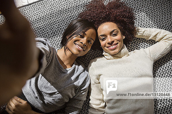 Portrait glücklicher Freundinnen  die zu Hause auf dem Teppich liegen