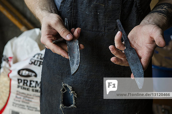 Mittelteil eines Schmiedes  der Messer hält  während er in der Werkstatt steht