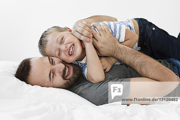 Cheerful father and son playing while lying on bed at home