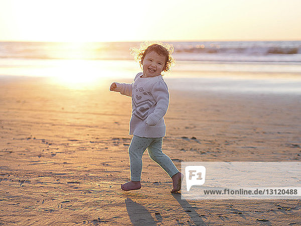 Happy baby girl running at beach against clear sky during sunset