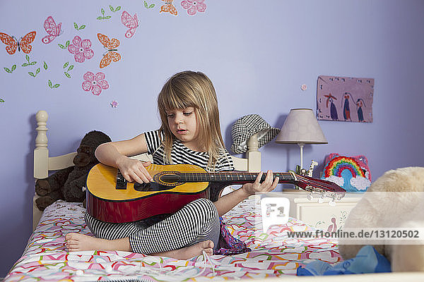 Mädchen spielt zu Hause im Bett Gitarre