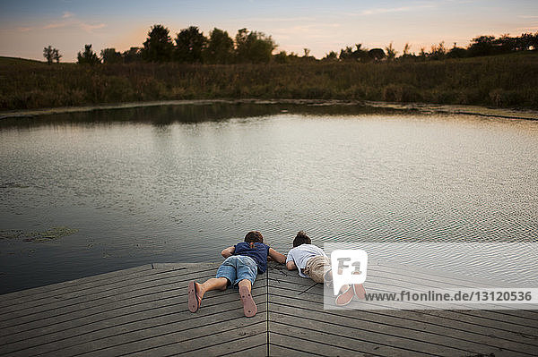 High angle view of siblings lying on pier over lake at park