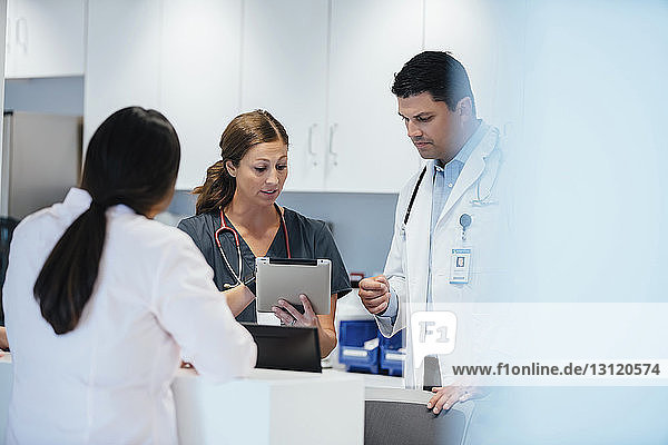 Nurse showing tablet computer to colleague with female doctor standing in foreground