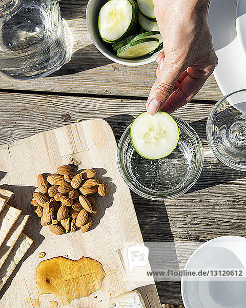 Cropped image of hand holding cucumber slice over glass by food tray on table