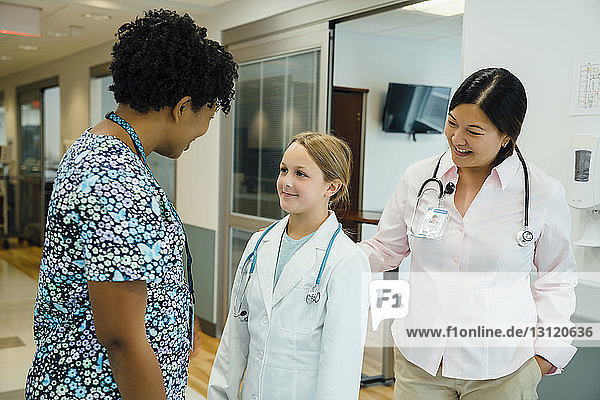 Girl wearing lab coat while looking at pediatrician in hospital corridor