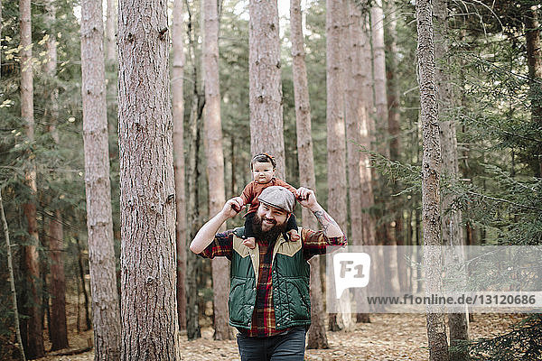Glücklicher Vater trägt seine Tochter beim Waldspaziergang auf den Schultern