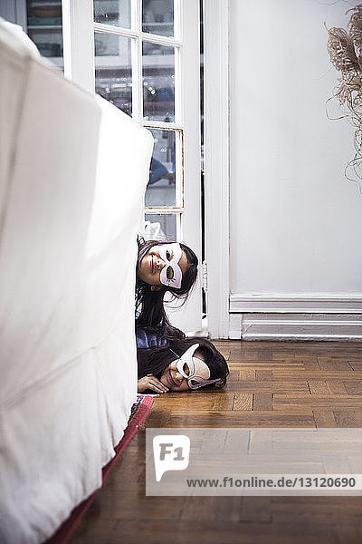 Porträt von Schwestern mit Augenmasken  die zu Hause am Sofa vorbeischauen