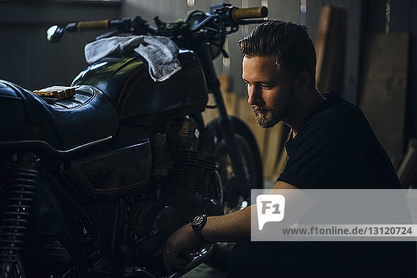 Thoughtful man crouching by motorcycle in garage