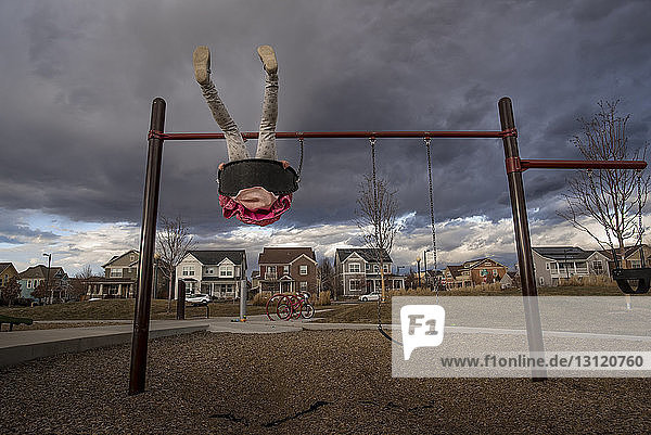 Niedrige Sektion eines verspielten Mädchens  das auf der Schaukel gegen stürmische Wolken auf dem Spielplatz schaukelt