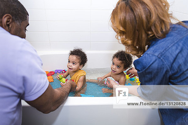 Parents bathing daughters together in bathtub