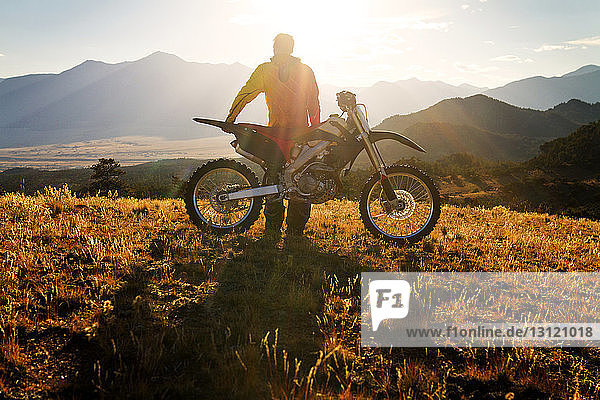 Rear view of biker standing by dirt bike on mountain