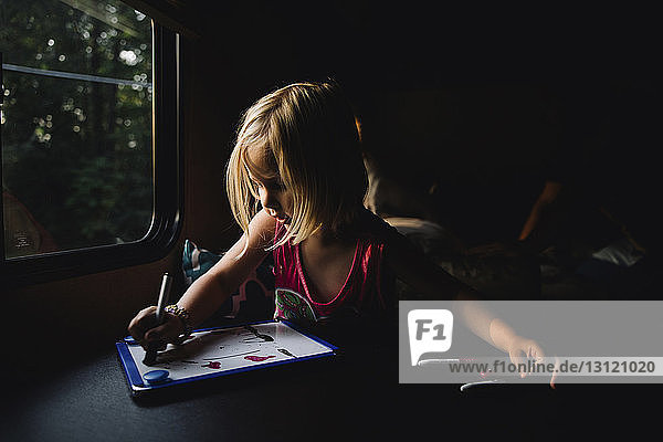 Mädchen zeichnet auf Schiefertafel  während sie zu Hause in der Dunkelkammer sitzt