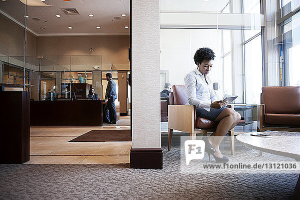 Geschäftsfrau benutzt Tablet-Computer  während sie im Büro auf dem Sofa sitzt