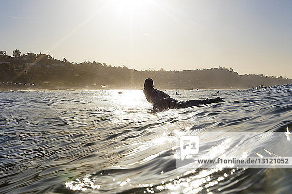 Weibliche Surferin liegt bei Sonnenuntergang auf einem Surfbrett im Meer