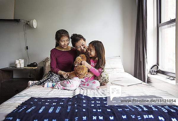 Mother playing with happy daughters on bed at home
