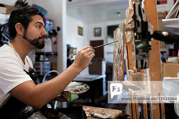 Side view of painter painting on canvas in art studio