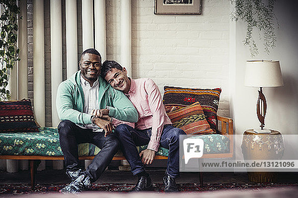 Full length portrait of loving gay couple sitting on chaise longue at home