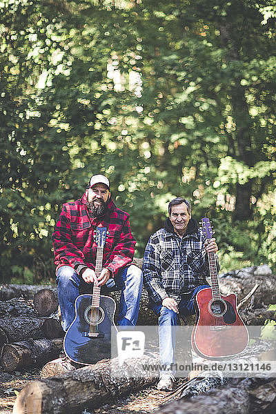 Portrait of friends with guitars sitting on logs in forest