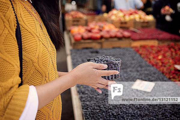 Midsection of woman holding blueberries at market stall