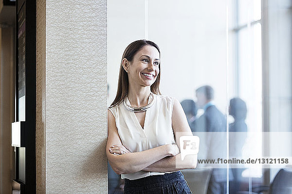 Happy businesswoman leaning on wall in office
