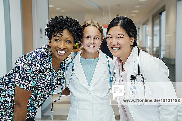 Portrait of cheerful female doctors with girl wearing lab coat in hospital