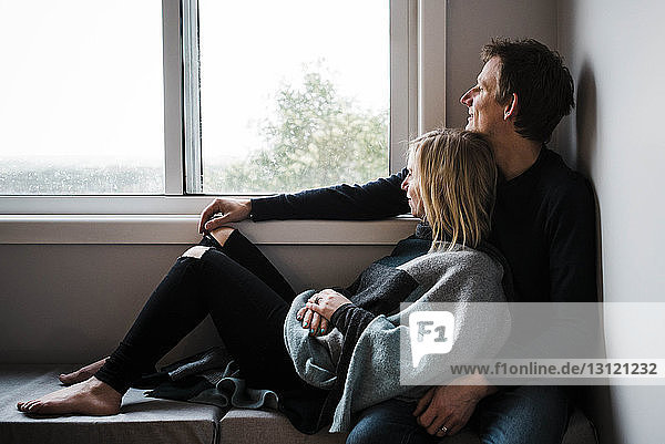 Thoughtful loving couple looking through window while resting at home