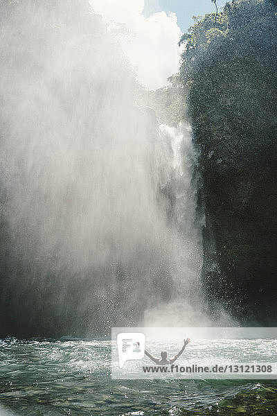 Rückansicht eines Mannes mit ausgestreckten Armen im Fluss am majestätischen Wasserfall