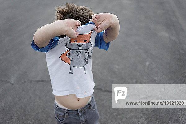 Hochwinkelansicht eines Jungen  der sein T-Shirt auszieht  während er auf einem Fußweg steht