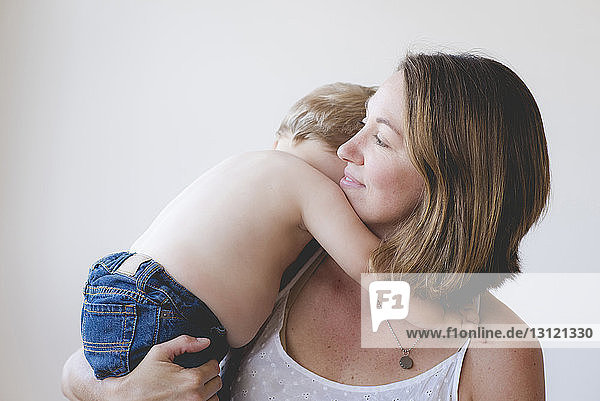 Thoughtful mother carrying shirtless son against white background