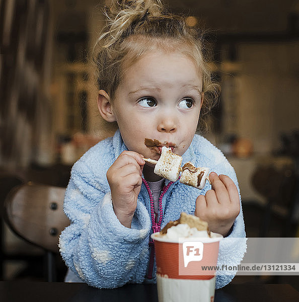Nahaufnahme eines Mädchens  das Marshmallow isst  während es im Restaurant am Tisch sitzt