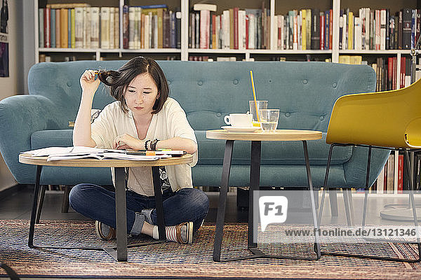 Junge Frau studiert in voller Länge  während sie zu Hause am Sofa auf einem Teppich sitzt