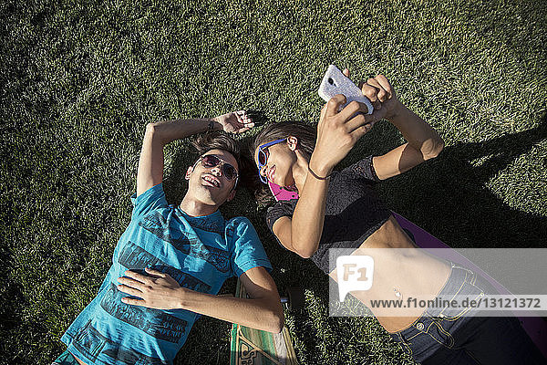 Overhead view of woman taking selfie with friend lying on grassy field