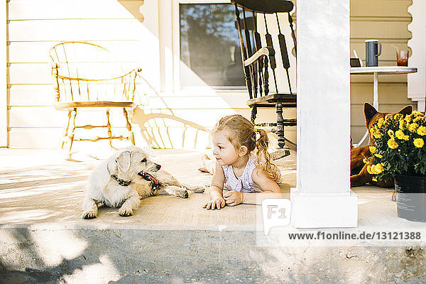 Mädchen liegt mit Hund auf der Veranda