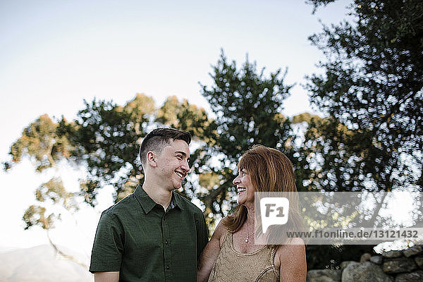 Niedrigwinkelansicht eines glücklichen Sohnes und einer glücklichen Mutter  die sich gegenseitig ansehen  während sie im Park an Bäumen stehen
