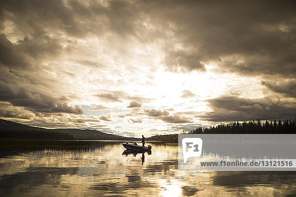 Distant view of father and son in boat on lake against cloudy sky during sunset