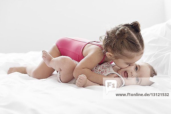 Girl kissing sister lying on bed at home