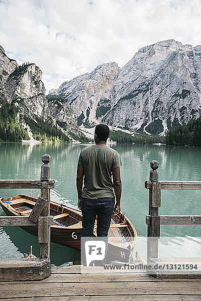 Mann schaut auf Ansicht  während er an einem Holzgeländer am See gegen Berge steht