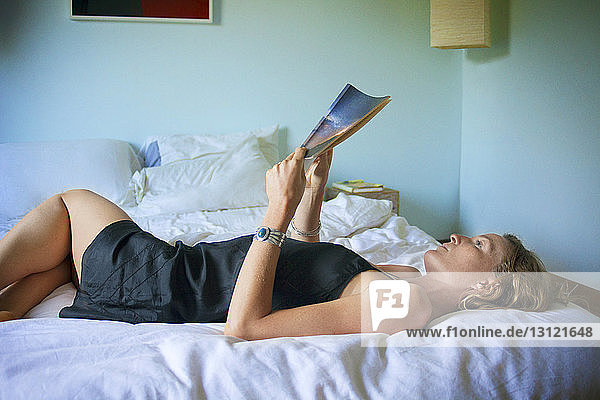 Frau liest Buch  während sie zu Hause im Bett liegt
