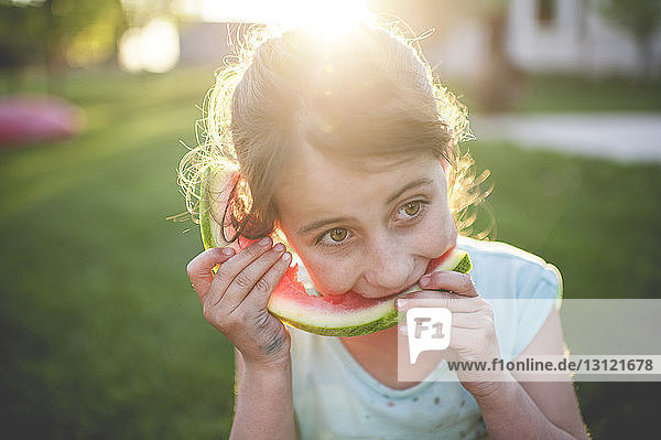Mädchen isst Wassermelone  während sie auf einem Grasfeld sitzt