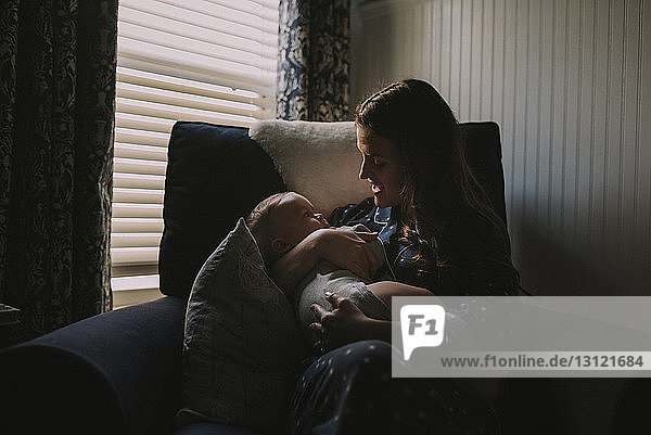 Mother with son sitting on armchair by window at home