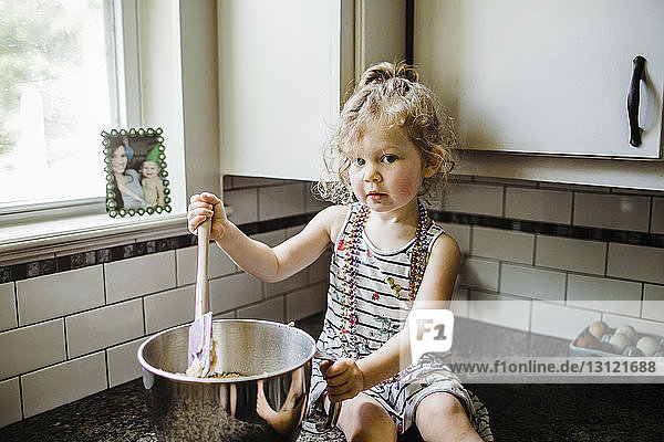 Porträt eines süßen Mädchens  das in einem Behälter Essen zubereitet  während es zu Hause auf der Küchentheke sitzt