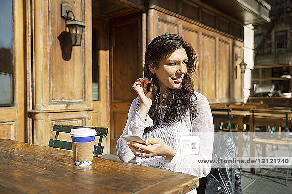 Nachdenkliche Frau hält Smartphone in der Hand  während sie im Straßencafé sitzt