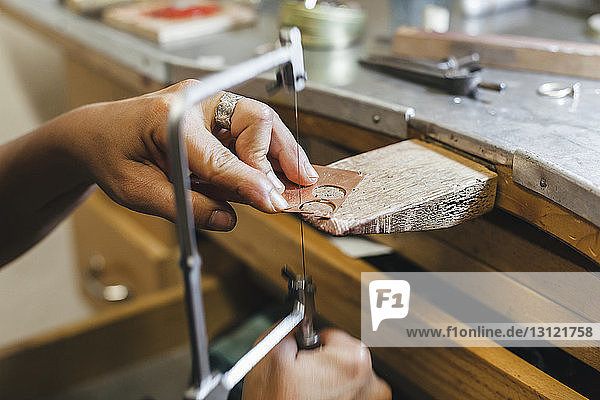 Geschnittene Hände einer Handwerkerin mit einer Handsäge bei der Arbeit am Tisch in der Werkstatt