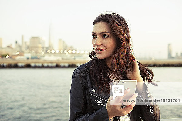 Nachdenkliche Frau hält ein Smartphone mit dem One World Trade Center im Hintergrund