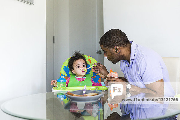 Vater füttert Tochter  während er am Tisch sitzt