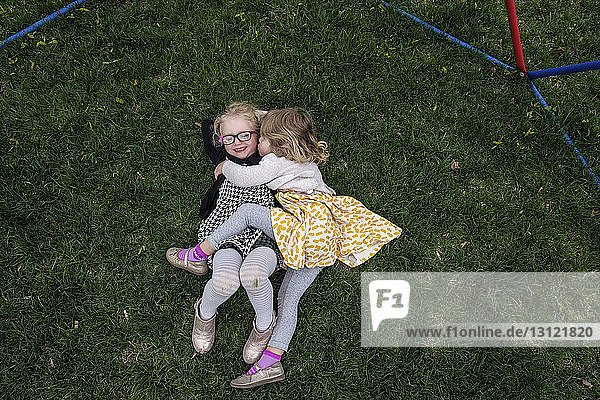 Hochwinkelansicht der glücklichen Schwestern  die auf einem Grasfeld im Hof liegen