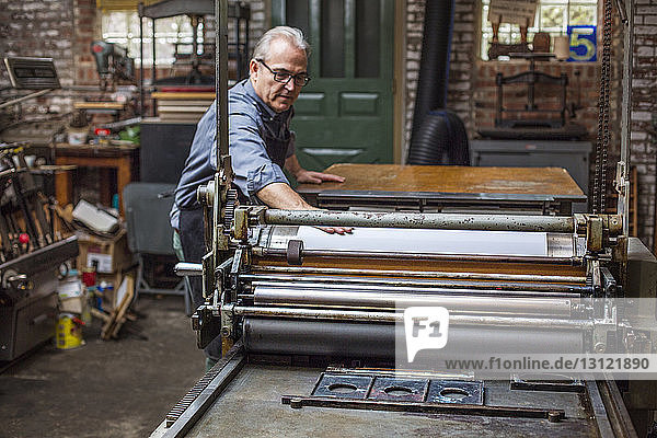 Man using printing press while standing at workshop